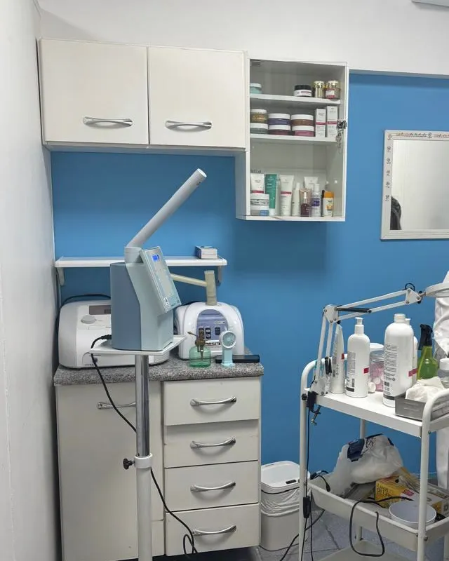 Sala de estética no mesmo andar, com aparelhos, armário de produtos e a parede azul